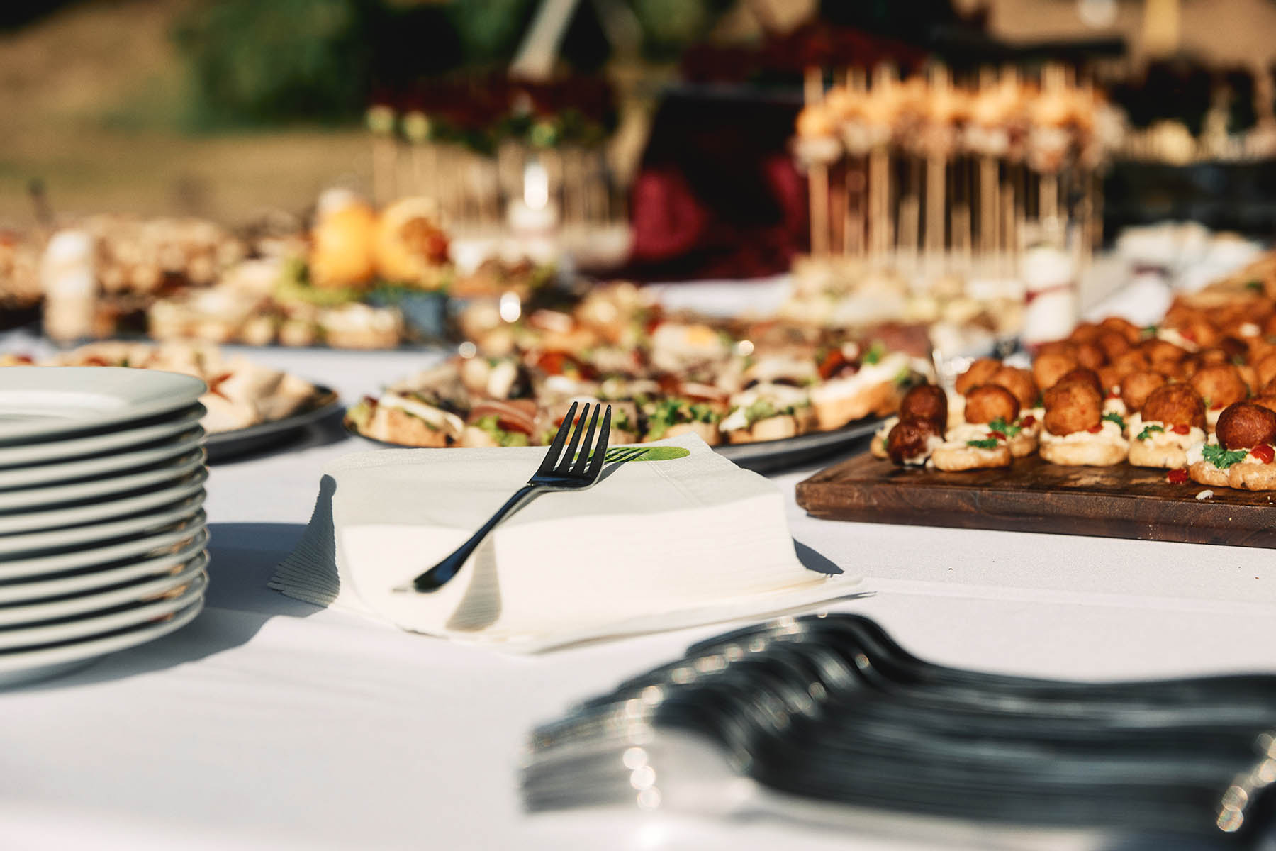 Focus on a fork on a napkin next to the served catering on an outdoor wedding day.